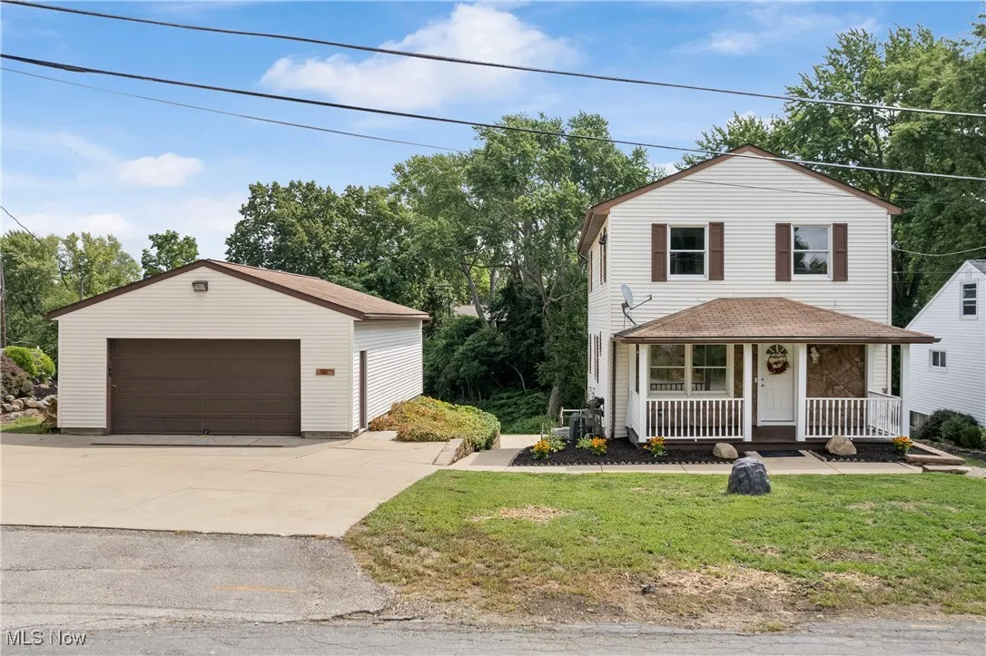 Traditional-style house with covered porch, a garage, an outdoor structure, a front lawn, and a shingled roof