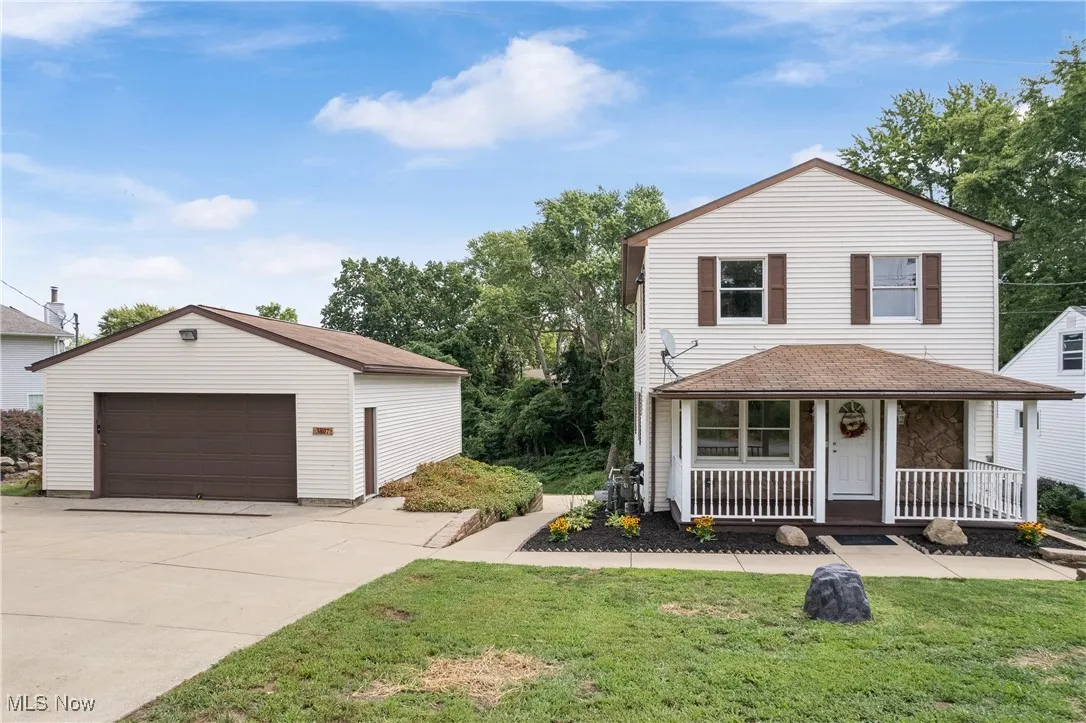 View of front of house featuring a porch, a detached garage, a front lawn, an outdoor structure, and stone siding
