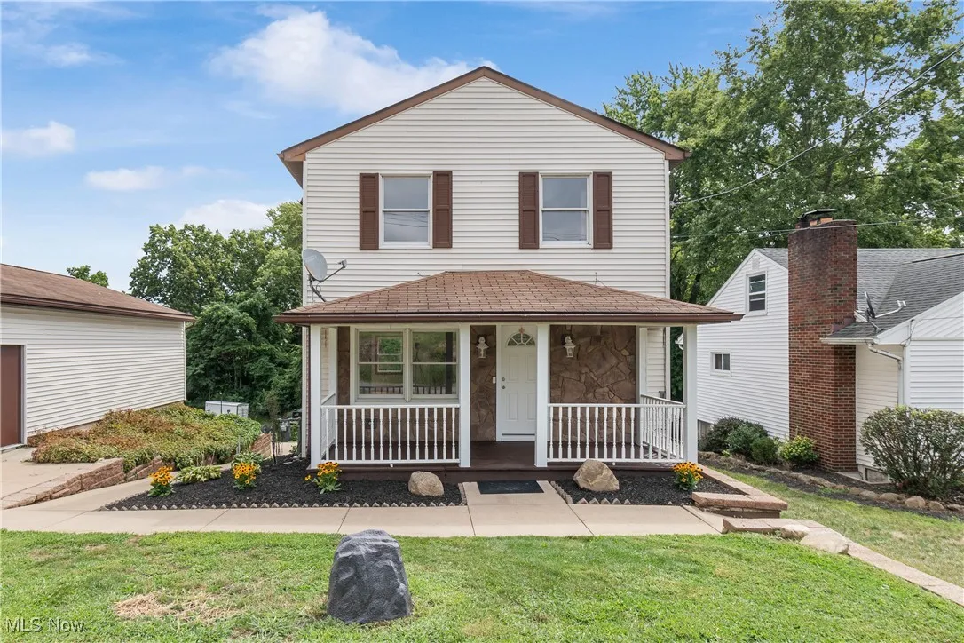 Traditional home featuring a front lawn, covered porch, and stone siding
