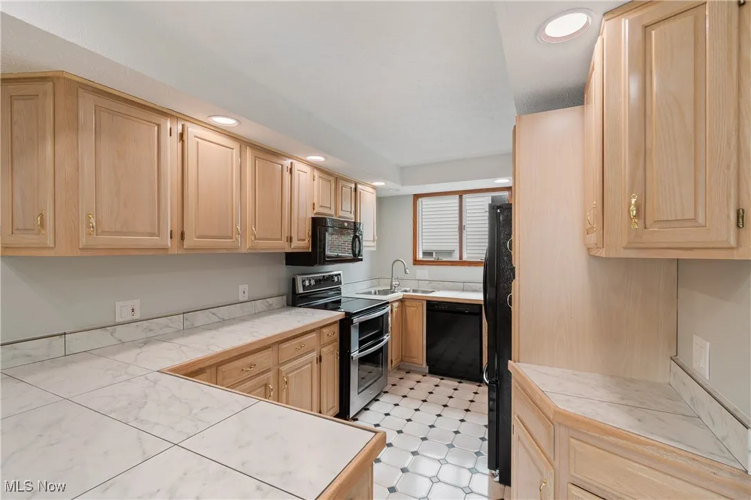 Kitchen featuring black appliances, light brown cabinets, and recessed lighting