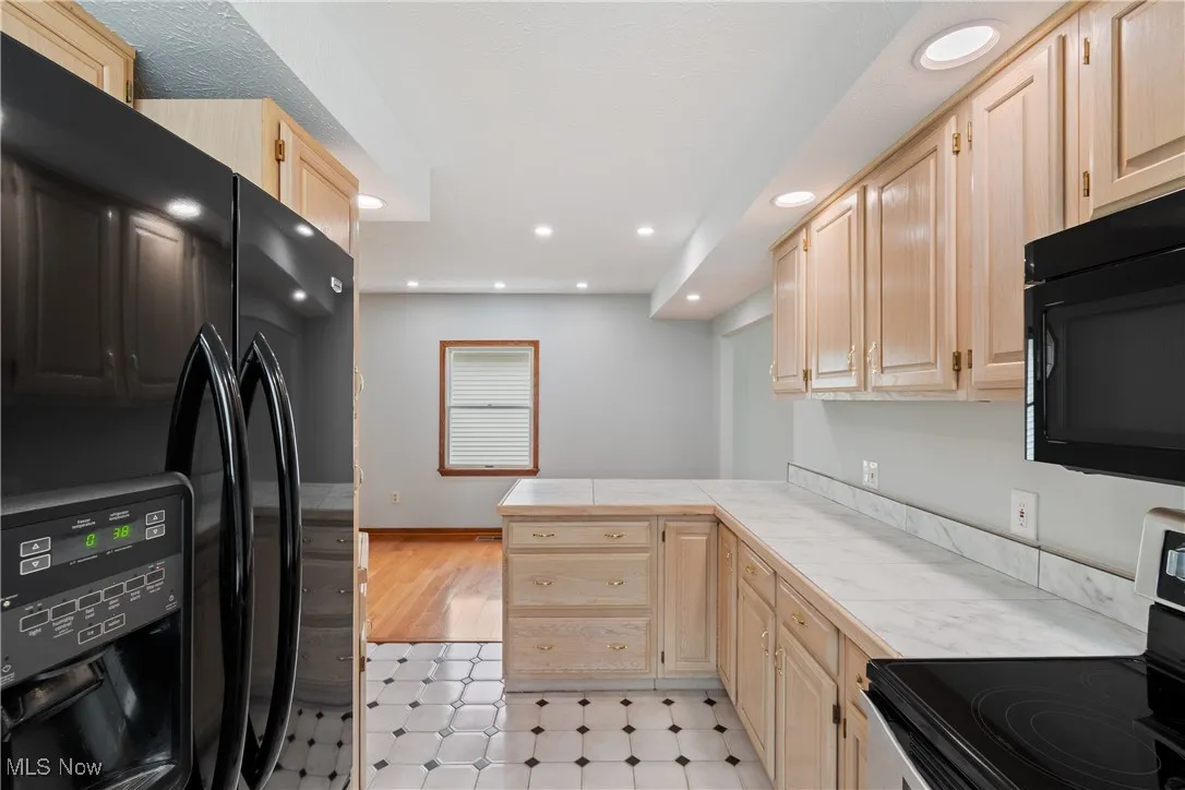 Kitchen with black appliances, light brown cabinets, recessed lighting, tile counters, and a peninsula