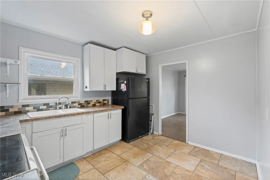 Kitchen featuring white cabinetry, black appliances, stone tile flooring, and tasteful backsplash