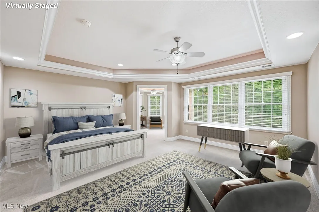 Carpeted bedroom featuring a raised ceiling, a ceiling fan, and recessed lighting and a sitting area