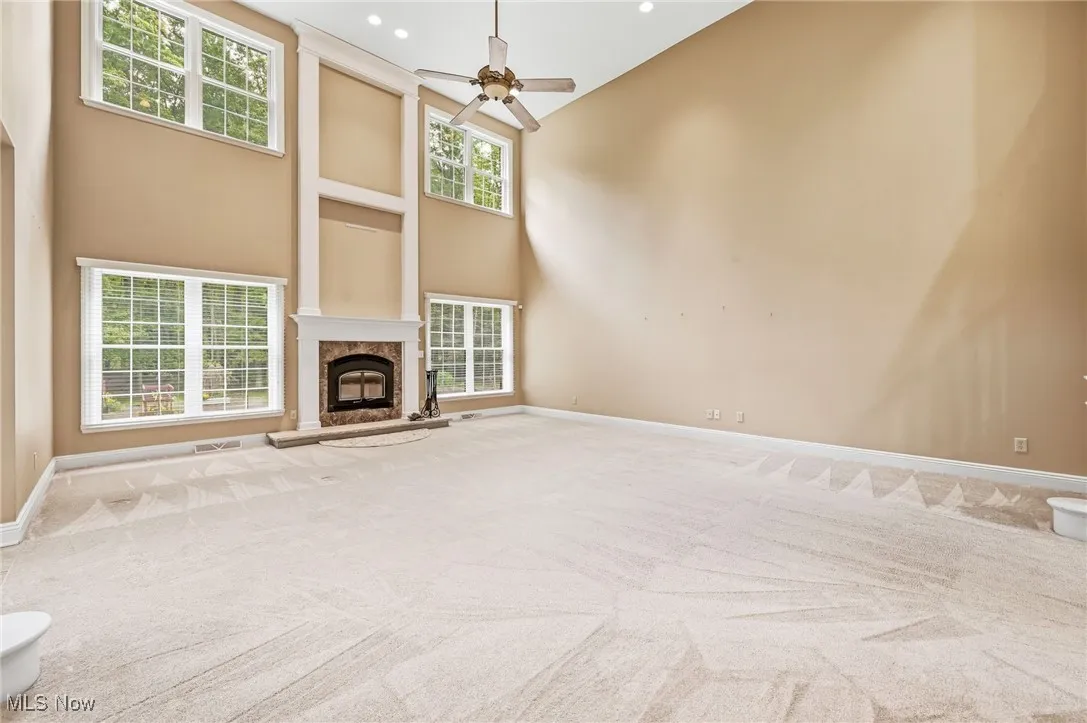 Unfurnished living room with a towering ceiling, carpet floors, a premium fireplace, a ceiling fan, and recessed lighting