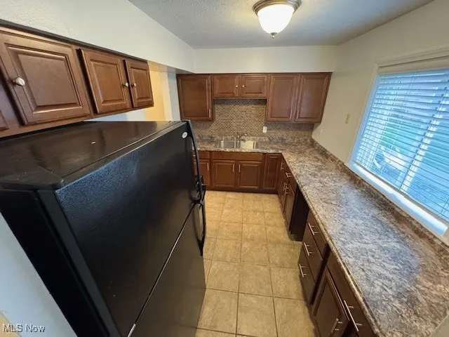 Kitchen featuring black refrigerator, tasteful backsplash, light tile patterned flooring, and a textured ceiling