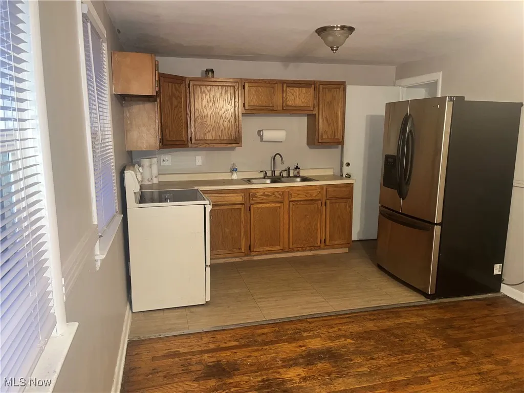 Kitchen featuring stainless steel refrigerator with ice dispenser, light countertops, electric range, brown cabinets, and light wood-style floors