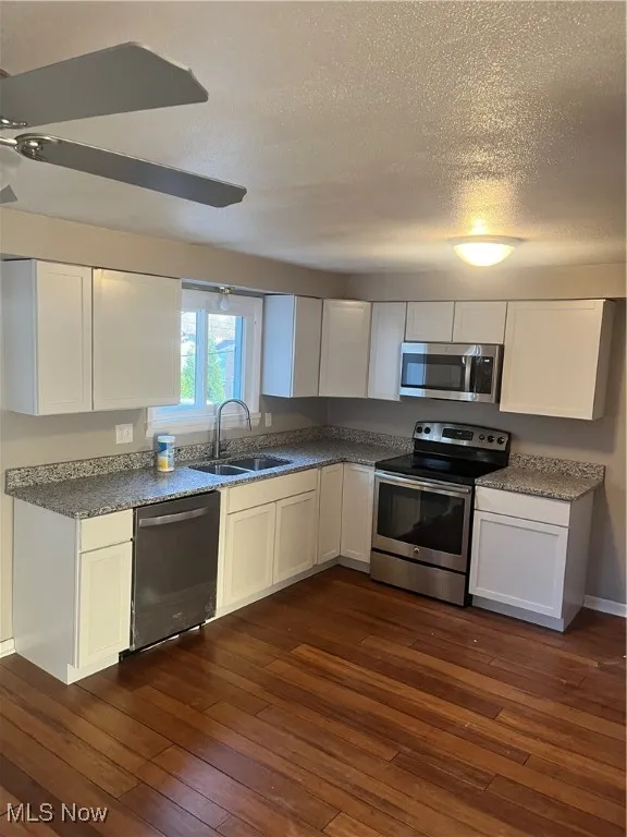 Kitchen with white cabinets, stainless steel appliances, a textured ceiling, dark wood-style flooring, and dark stone countertops