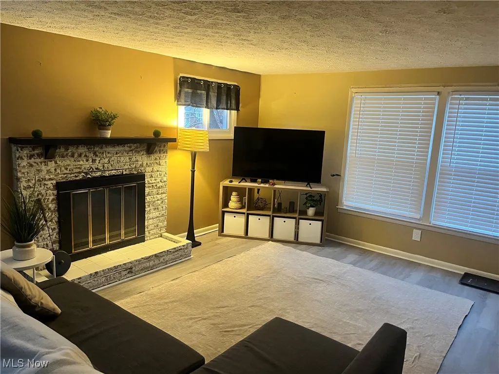 Living area featuring wood finished floors, a textured ceiling, and a glass covered fireplace