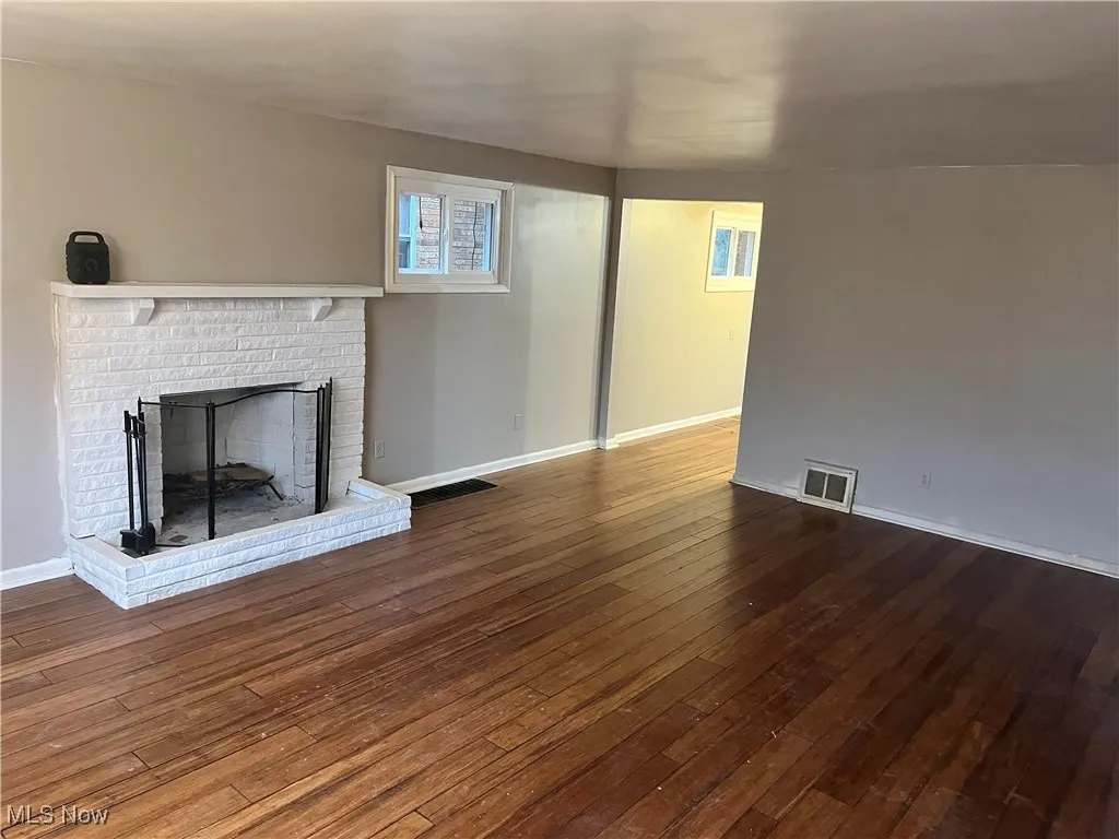 Unfurnished living room featuring dark wood-type flooring and a brick fireplace