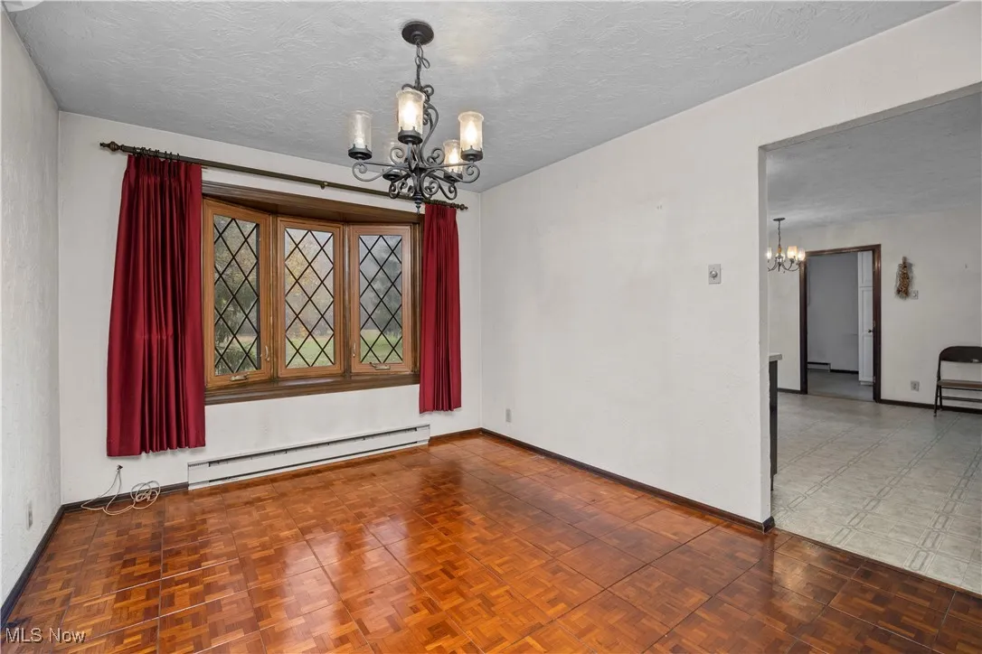 Unfurnished dining area with a chandelier, a baseboard heating unit, and a textured ceiling