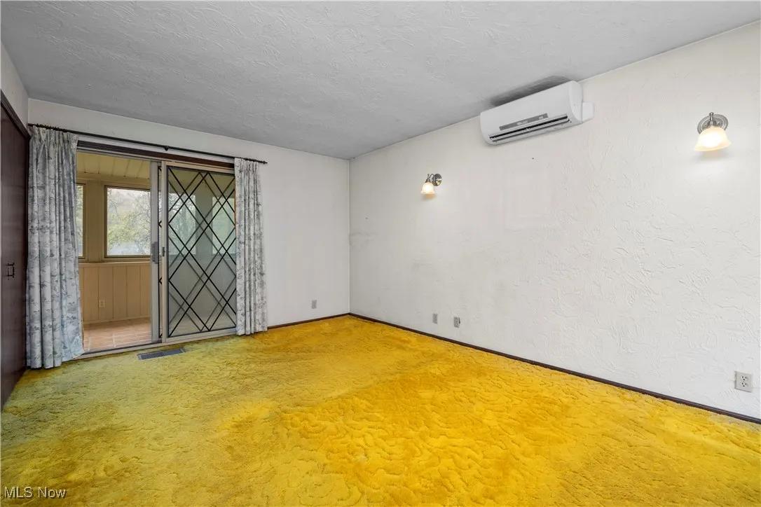 Carpeted master with a textured ceiling, a wall unit AC, and a textured wall