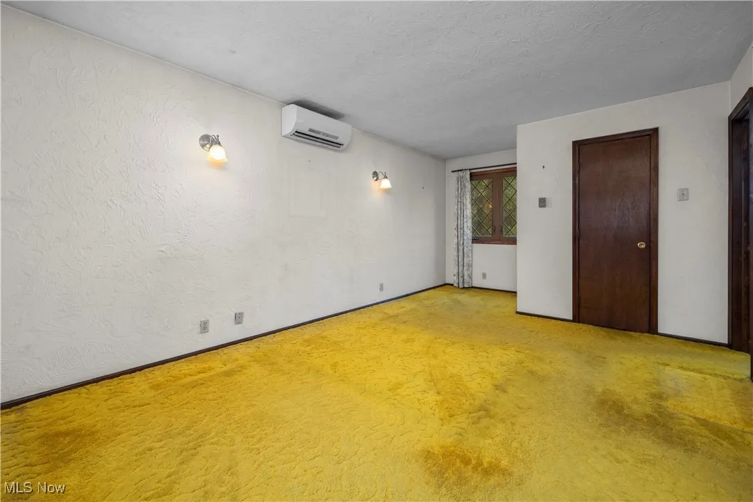master bedroom featuring a textured wall, a textured ceiling, carpet floors, and a wall unit AC