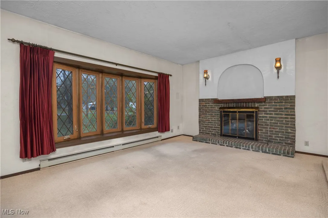 Unfurnished living room with a baseboard, a brick fireplace, carpet, large window and a textured ceiling