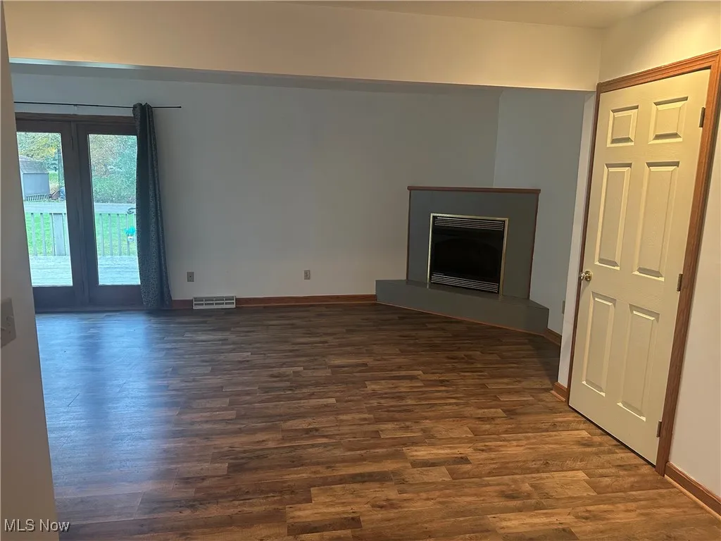 Unfurnished living room featuring a fireplace with raised hearth and dark wood-style flooring
