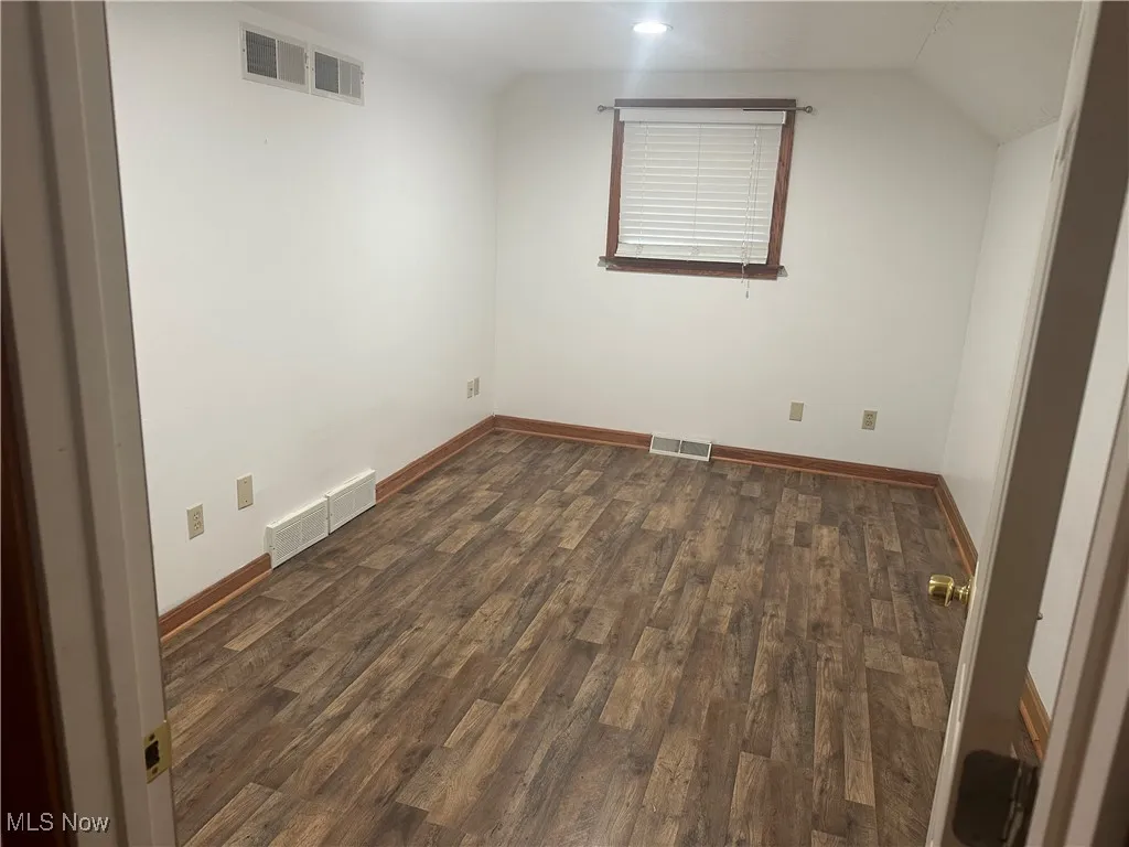 Empty room with dark wood finished floors and lofted ceiling