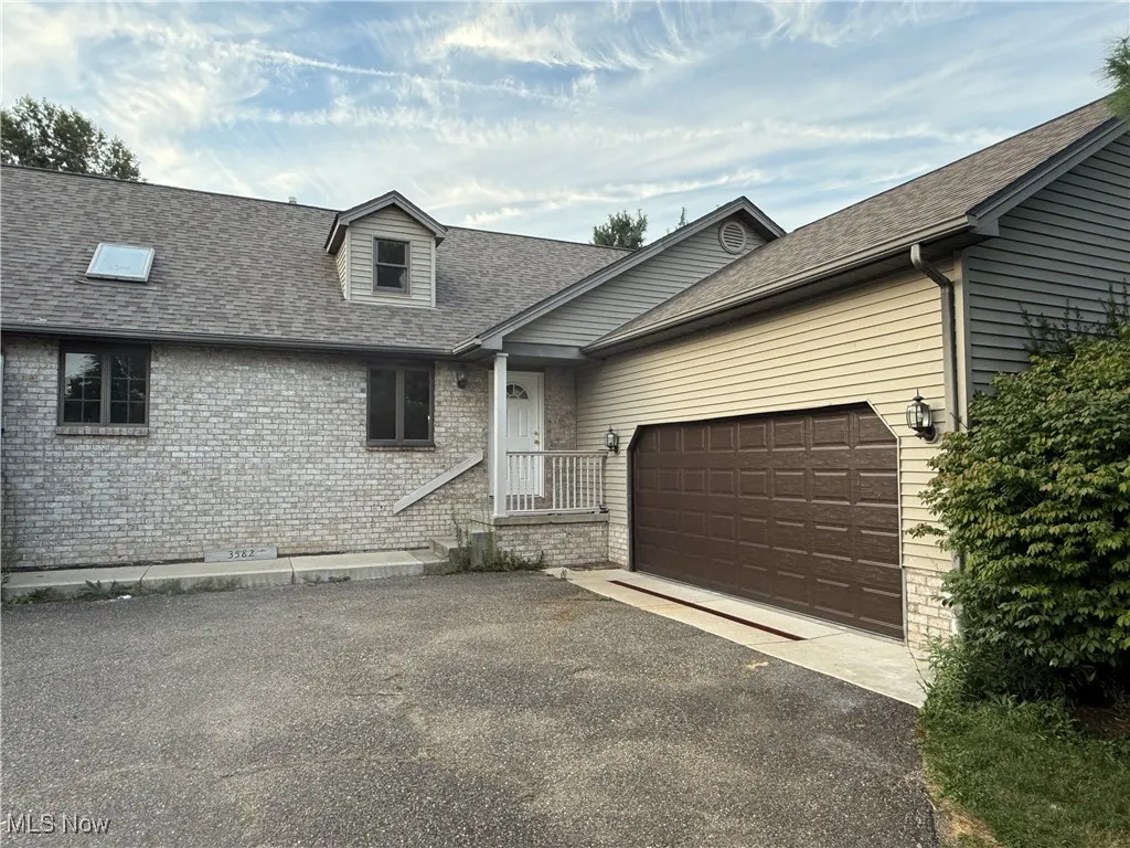 View of front of home featuring a shingled roof, asphalt driveway, brick siding, and a garage