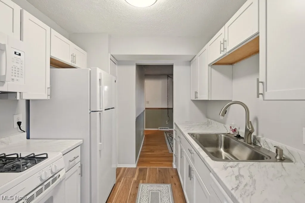 Kitchen with white cabinets, light wood-type flooring, white appliances, and a textured ceiling