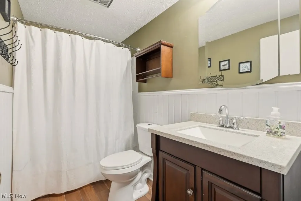 Bathroom featuring a textured ceiling, wainscoting, vanity, a shower with curtain, and light wood finished floors