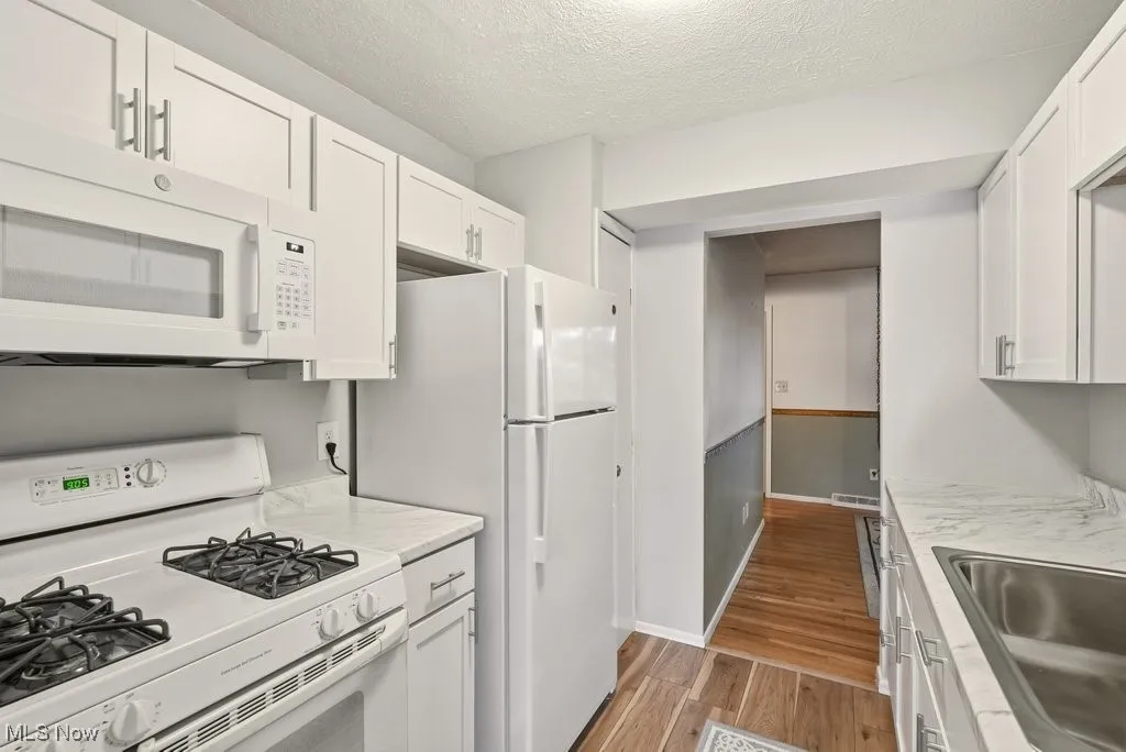 Kitchen with white appliances, light wood-style flooring, white cabinetry, light countertops, and a textured ceiling