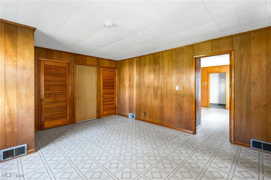 Unfurnished bedroom with wood walls, light flooring, and multiple closets