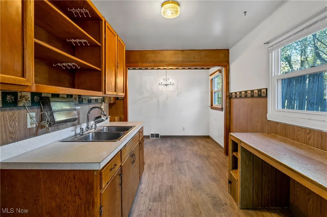 Kitchen featuring open shelves, brown cabinets, light wood-type flooring, wooden walls, and light countertops