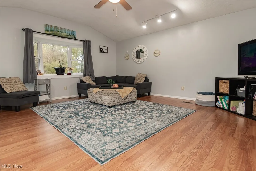 Living area with lofted ceiling, a ceiling fan, and light wood-style floors