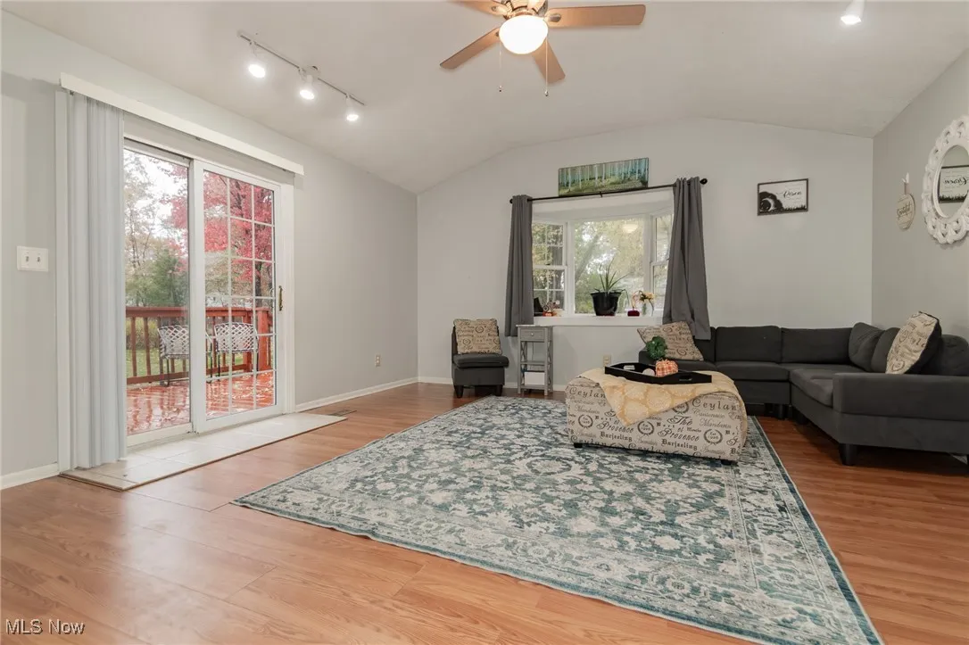 Living room featuring lofted ceiling, rail lighting, light wood finished floors, and a ceiling fan
