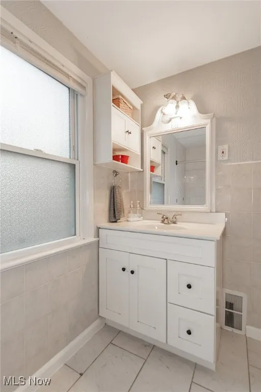 Full bathroom featuring tile walls, vanity, light marble finish floors, wallpapered walls, and a shower