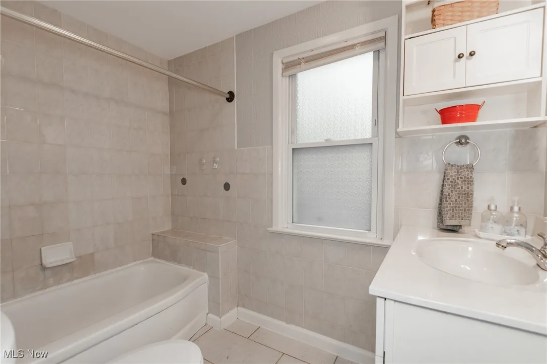Full bath featuring vanity, tile walls, washtub / shower combination, and light tile patterned flooring