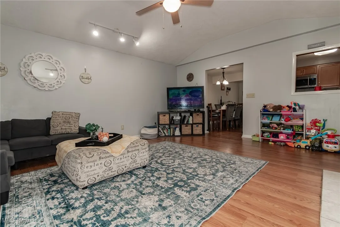 Living area featuring lofted ceiling, wood finished floors, a ceiling fan, a chandelier, and track lighting