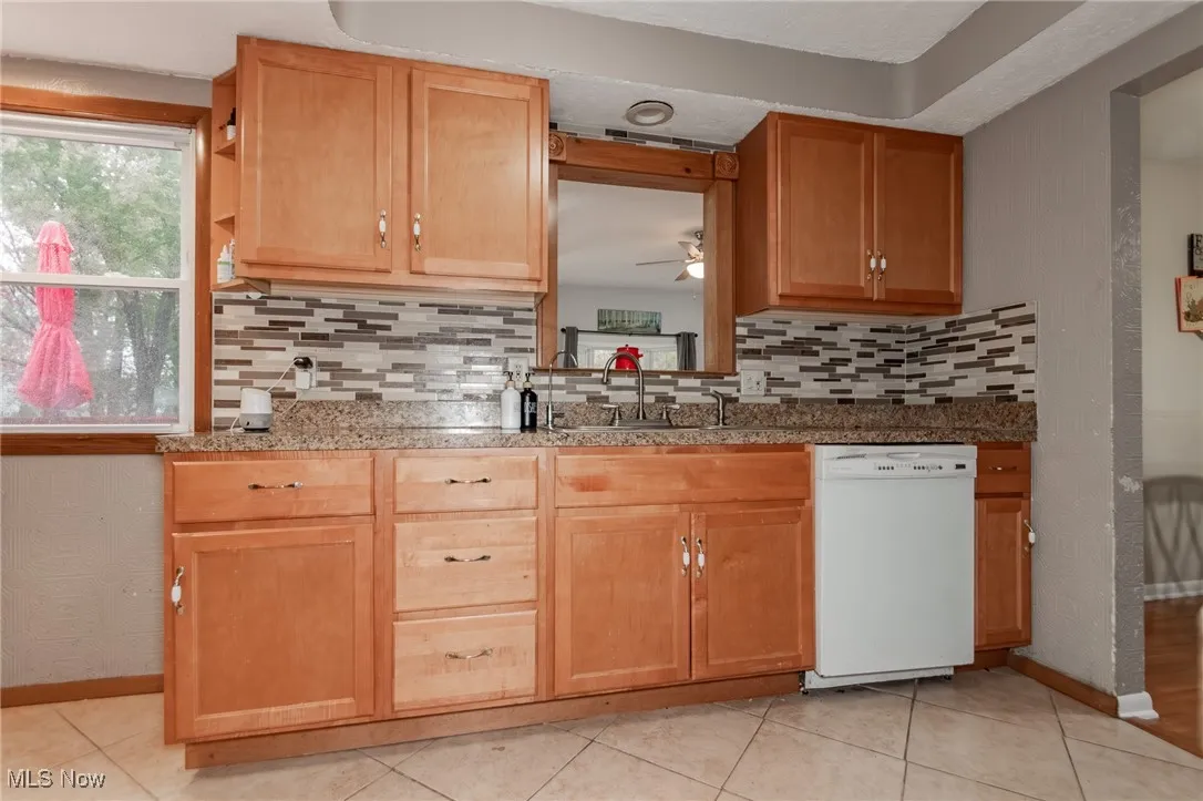 Kitchen featuring white dishwasher, light tile patterned flooring, and decorative backsplash