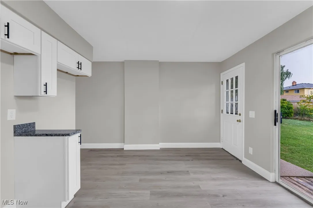 Kitchen with white cabinets, light wood finished floors, and dark stone countertops