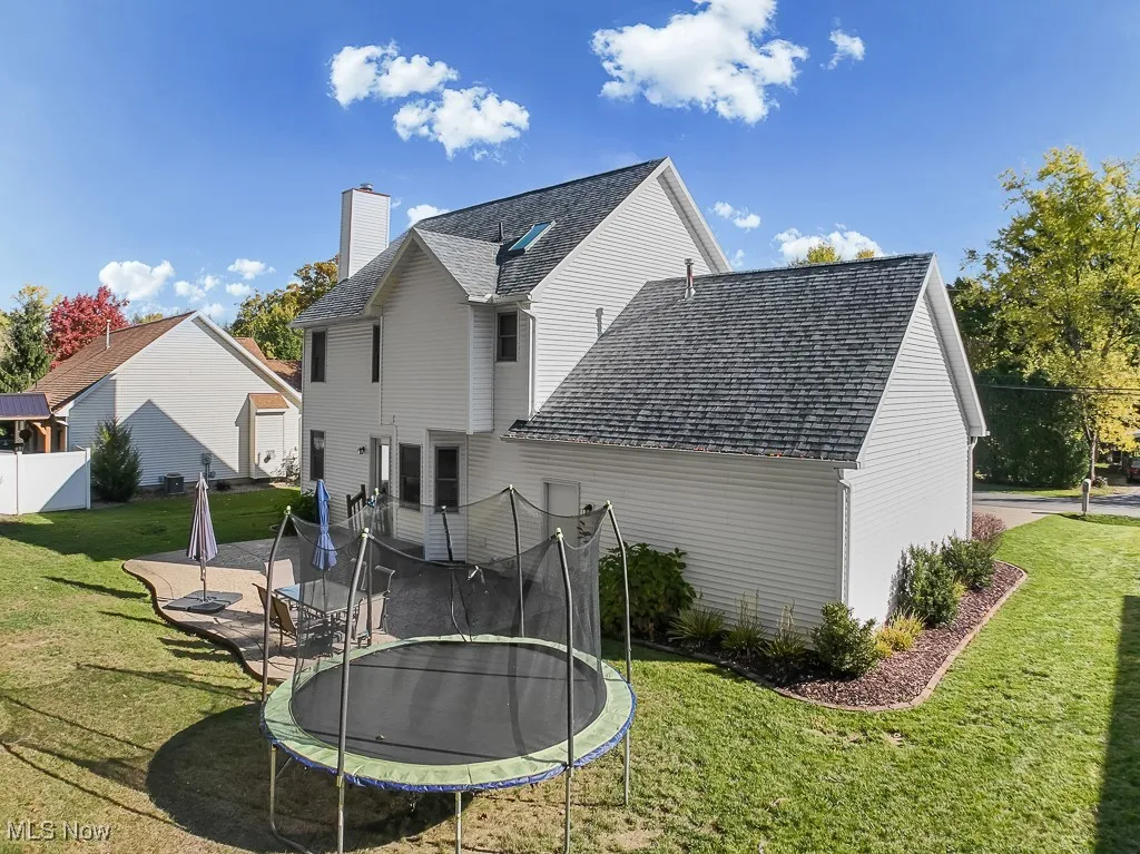 Back of property with a trampoline, a shingled roof, and a patio