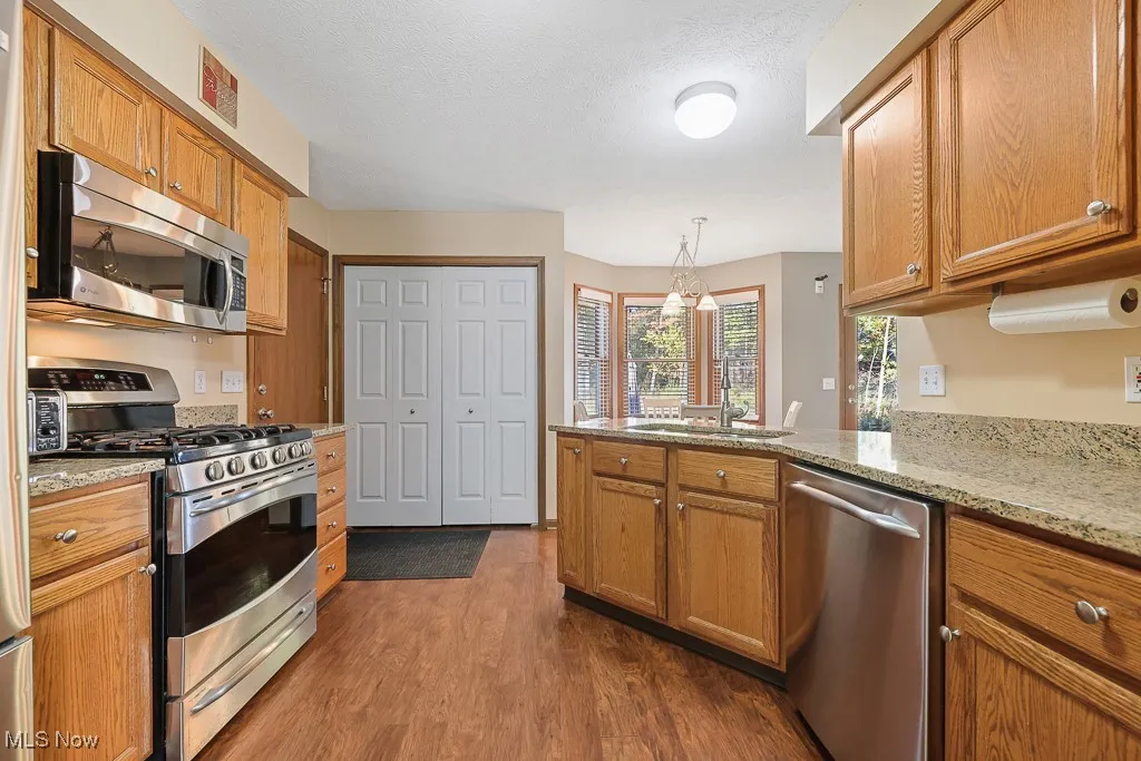 Kitchen with stainless steel appliances, dark wood-type flooring, brown cabinetry, and a textured ceiling