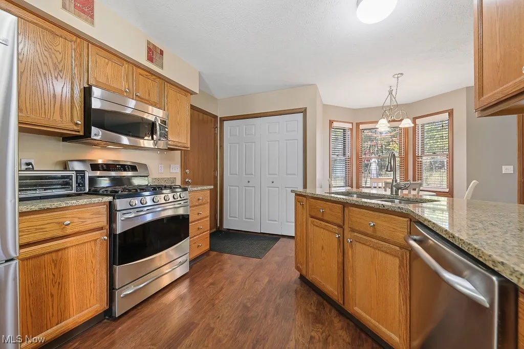 Kitchen with appliances with stainless steel finishes, dark wood-style flooring, brown cabinetry, light stone counters, and a textured ceiling