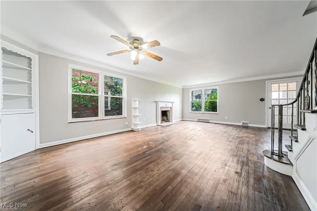 Unfurnished living room with stairway, dark wood-style flooring, ornamental molding, a fireplace, and a ceiling fan