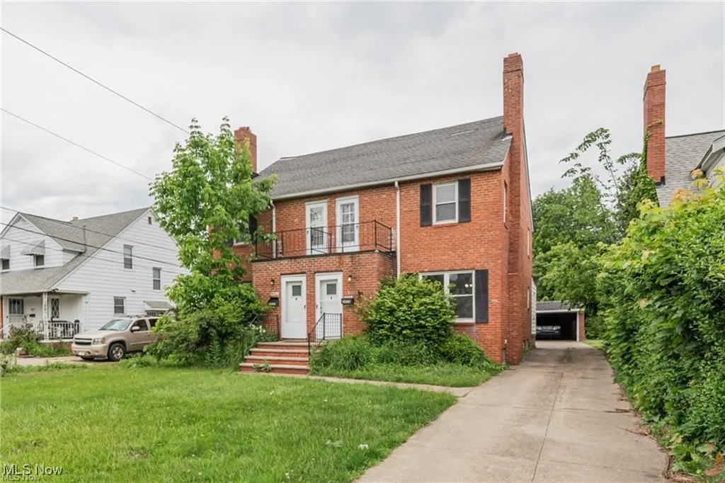 Colonial home with brick siding, a front yard, a chimney, and a balcony