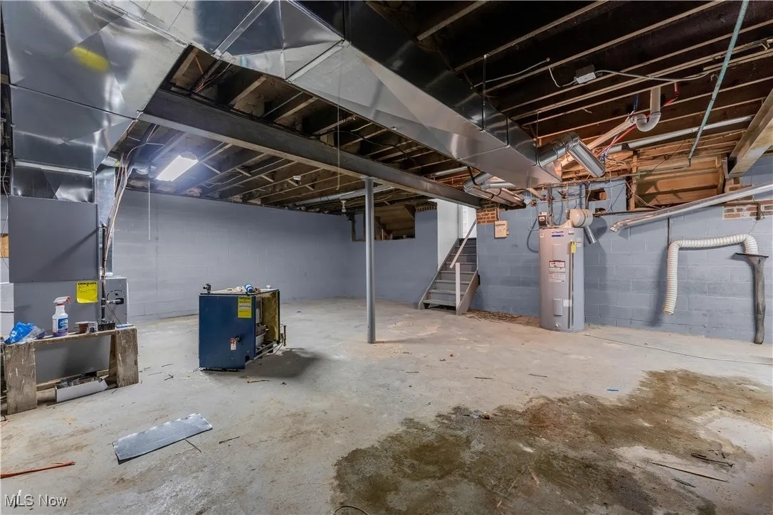 Unfinished below grade area featuring stairway, electric water heater, and heating unit