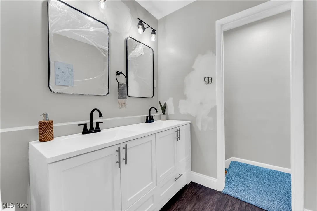 Full bathroom featuring double vanity and dark wood-type flooring