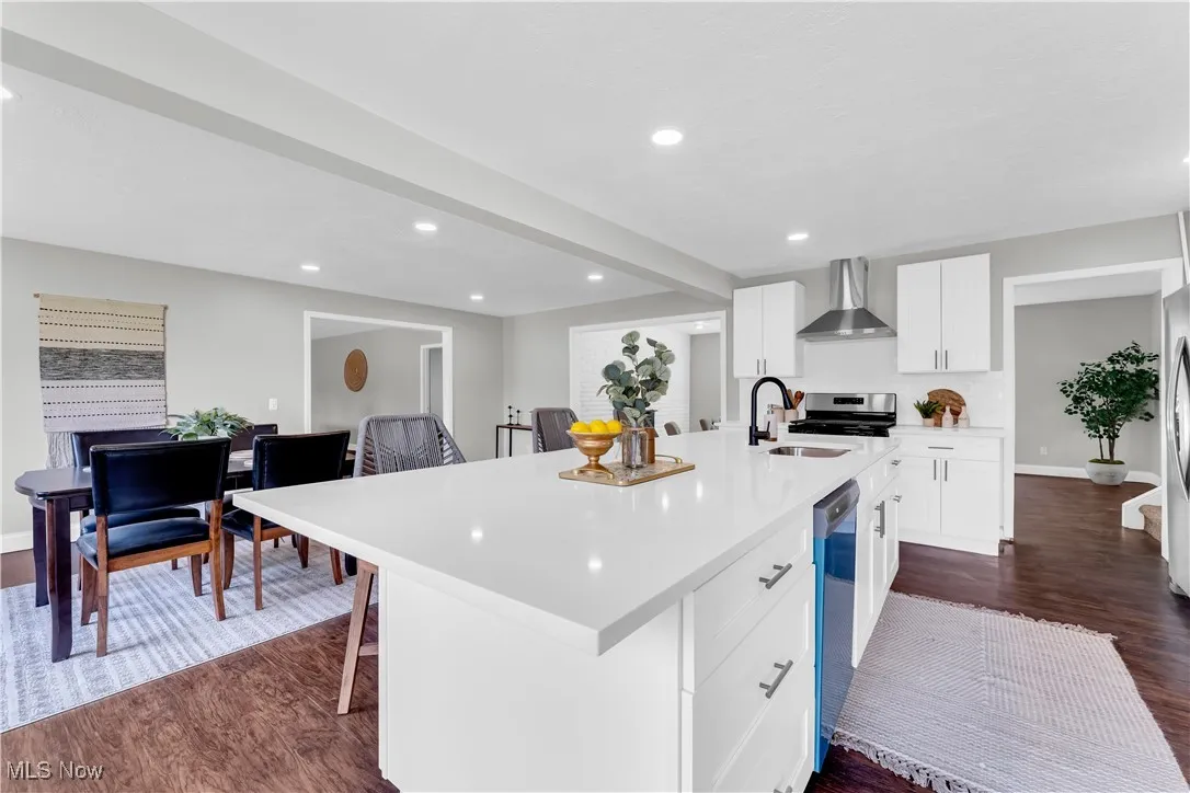 Kitchen featuring dark wood-style floors, white cabinetry, an island with sink, wall chimney exhaust hood, and recessed lighting