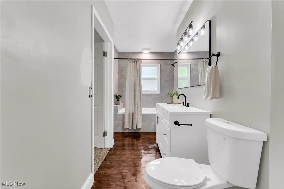 Bathroom with vanity, shower / tub combo with curtain, and dark wood-style flooring