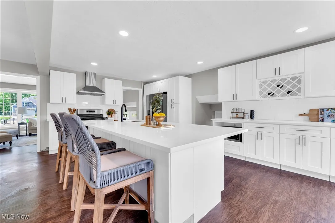Kitchen with a kitchen breakfast bar, white cabinets, wall chimney exhaust hood, an island with sink, and recessed lighting