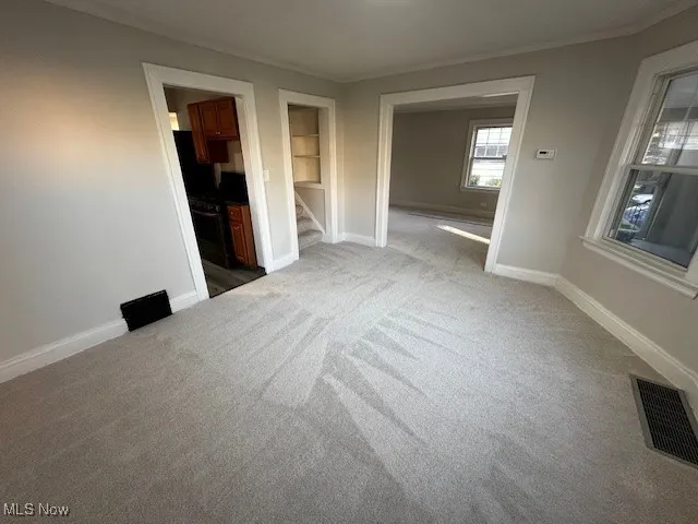 Unfurnished room featuring ornamental molding, light colored carpet, and stairs