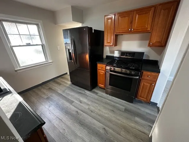Kitchen featuring dark countertops, stainless steel range with gas cooktop, brown cabinets, black fridge, and light wood-style flooring