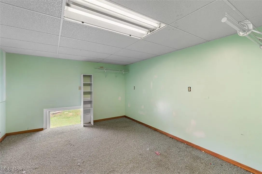 Carpeted spare room featuring baseboards and a drop ceiling
