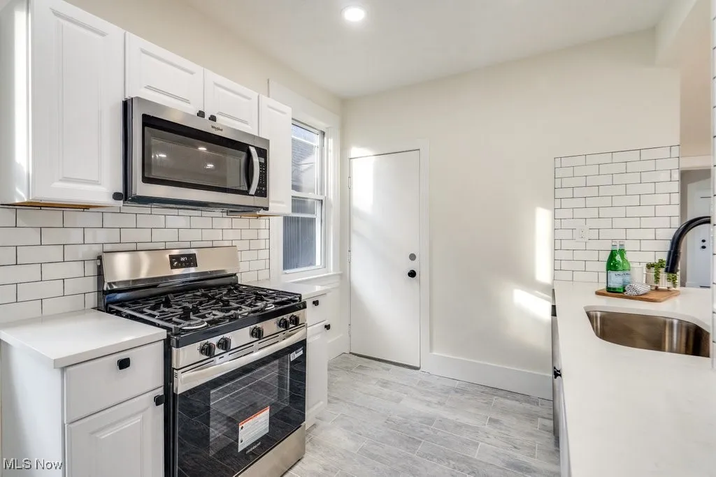 Kitchen with appliances with stainless steel finishes, backsplash, white cabinets, recessed lighting, and light wood-type flooring