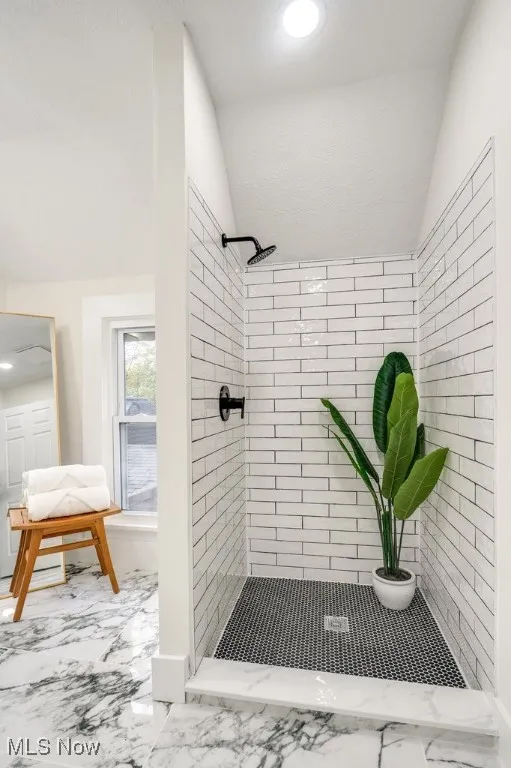 Bathroom with lofted ceiling, light marble finish floors, and a stall shower