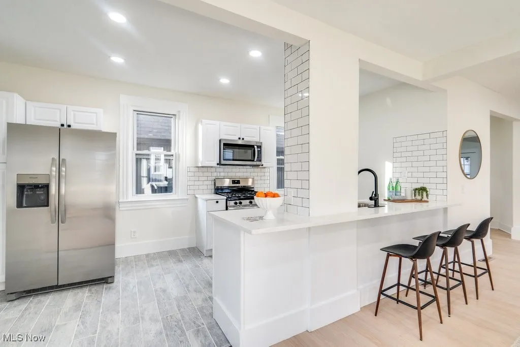 Kitchen with stainless steel appliances, tasteful backsplash, white cabinetry, light wood finished floors, and a kitchen bar