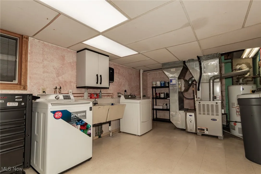 Washroom with light flooring, a paneled ceiling, washer and clothes dryer, water heater, and heating unit