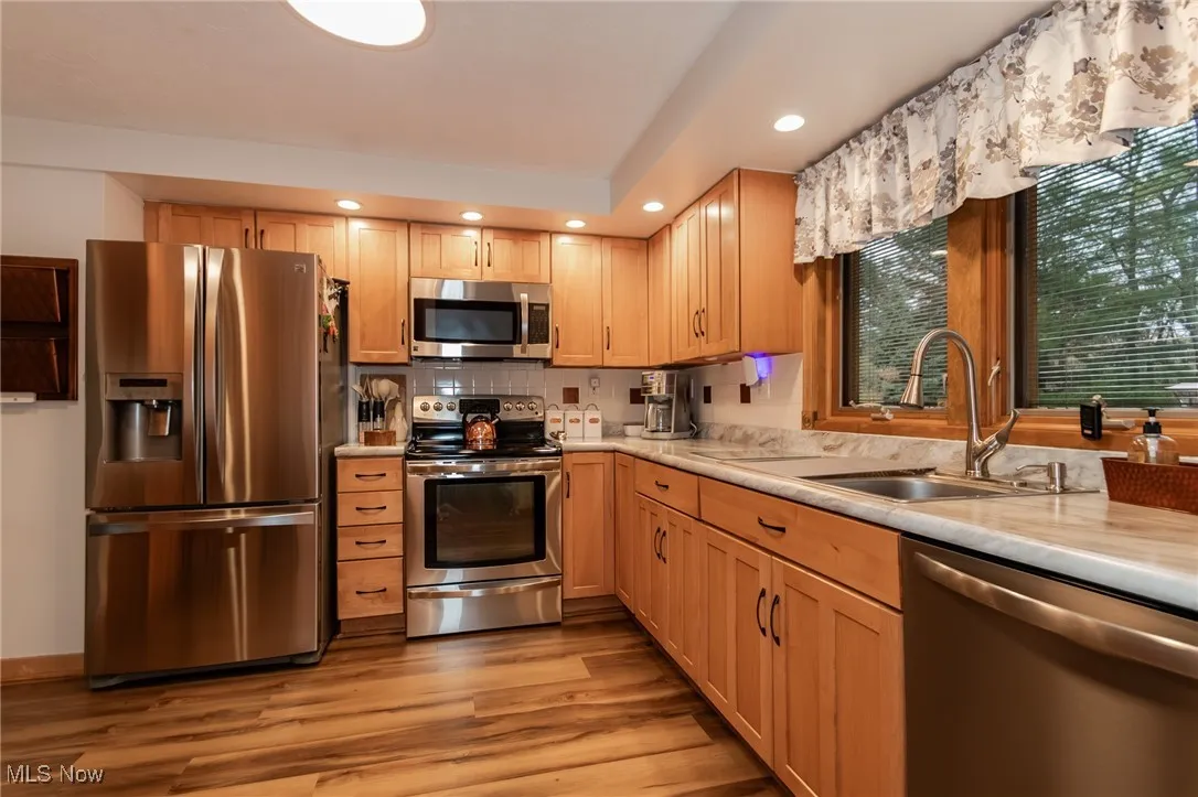 Kitchen with stainless steel appliances, light countertops, decorative backsplash, light wood-style floors, and recessed lighting